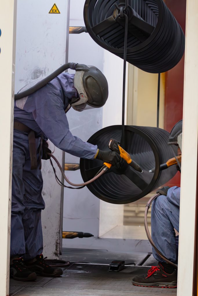 Ein Mann beschichtet mit einer Handmaschine gerade mehrere schwarze runde Serienteile.