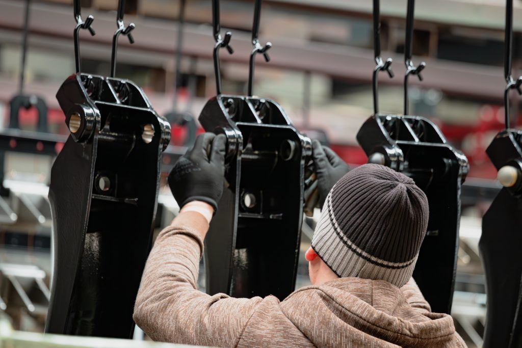 Pulverbeschichtete Teile werden von einem Mitarbeiter mit Mütze aufgehängt.