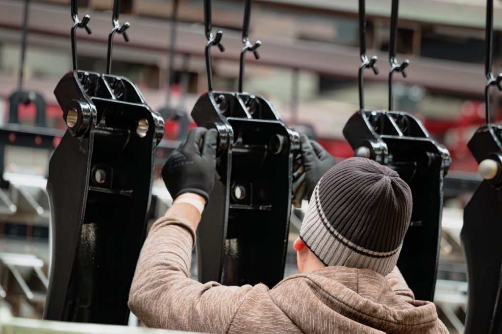 Pulverbeschichtete Teile werden von einem Mitarbeiter mit Mütze aufgehängt.