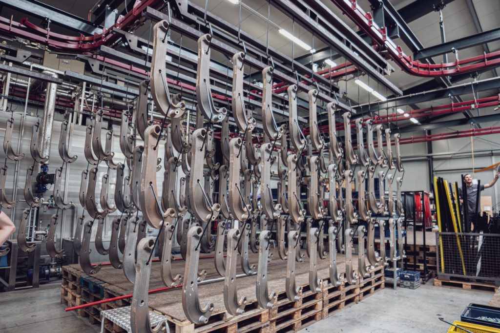 Viele längliche Teile hängen auf einer Halterung in einer Industriehalle.